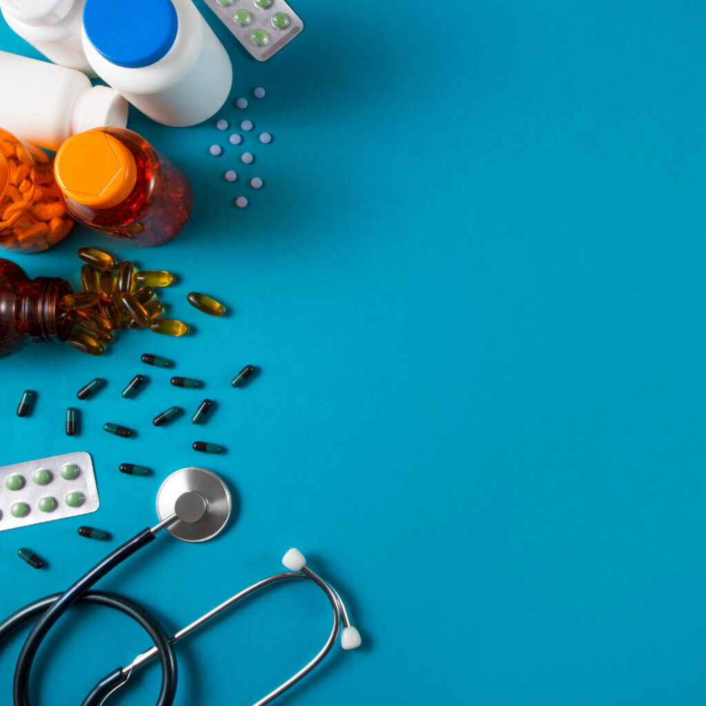 Assorted pill bottles, loose capsules and tablets, and a stethoscope arranged on a blue background.